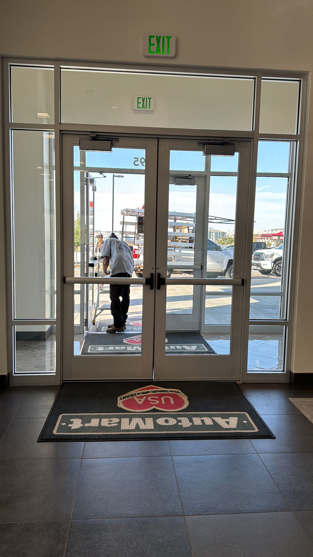 Person in white shirt and dark pants exiting a glass door with 