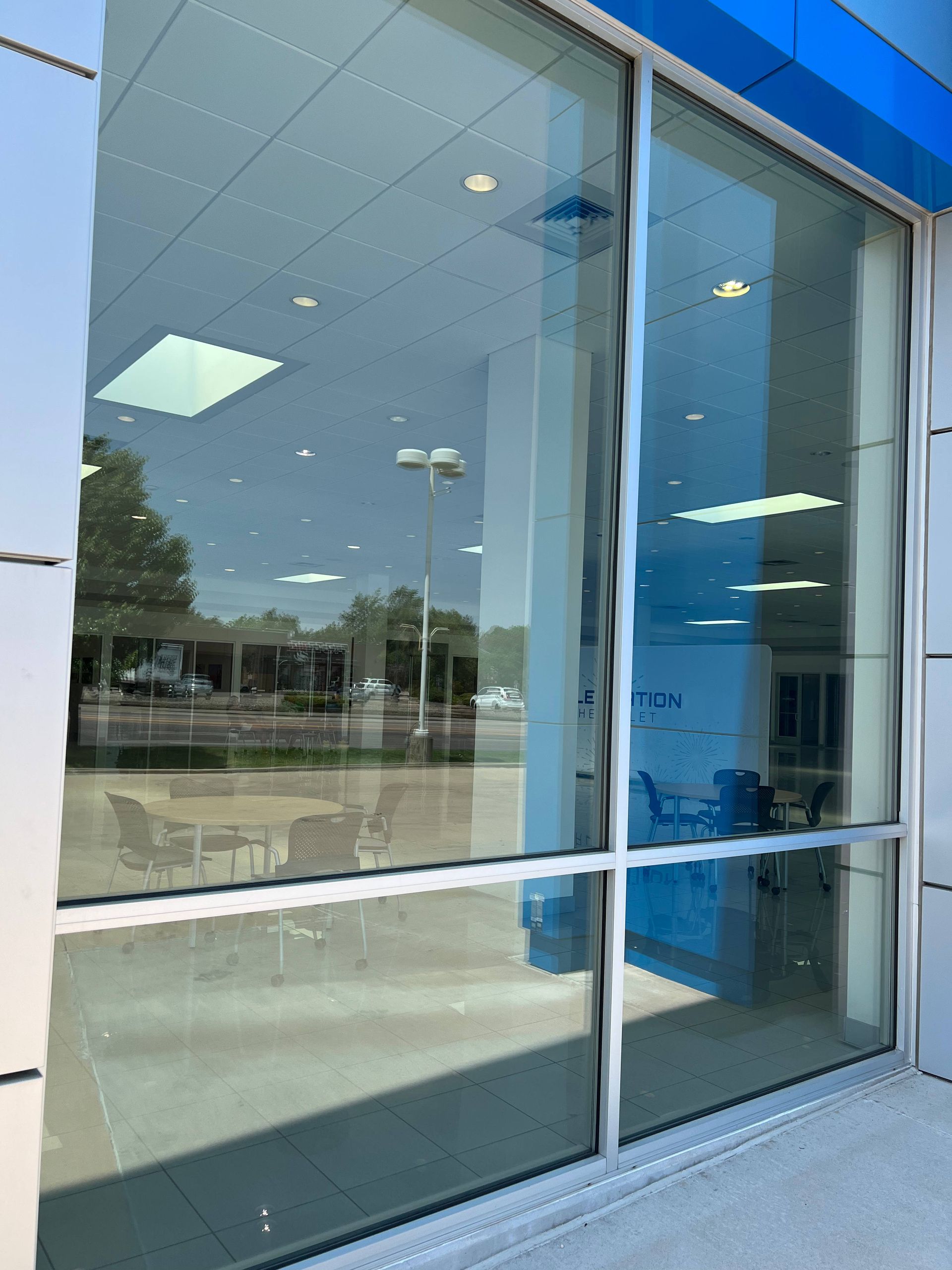 Large glass window reflecting a building interior, exterior, and sky. Blue tint.
