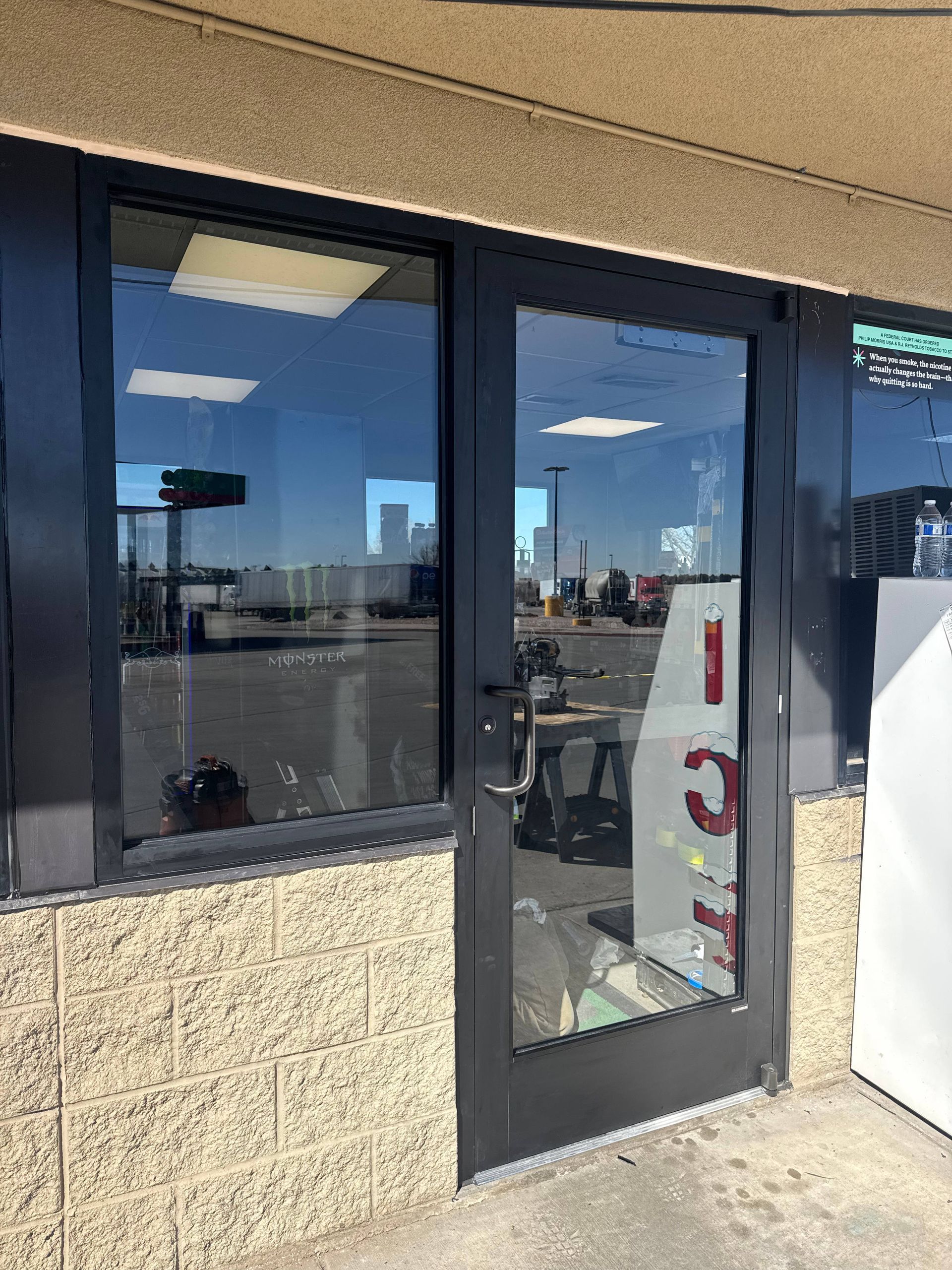 Black framed glass door slightly ajar, beige brick wall, reflective window, view of outdoors.