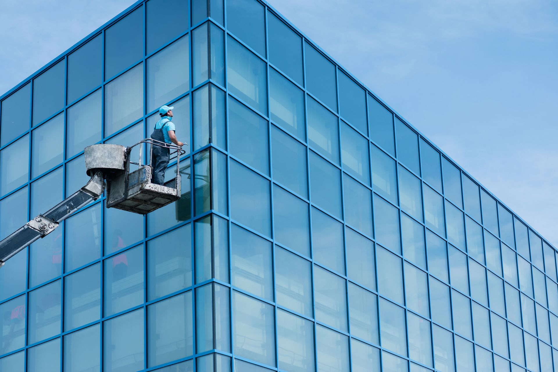 Worker on a lift cleaning the blue glass facade of a modern building