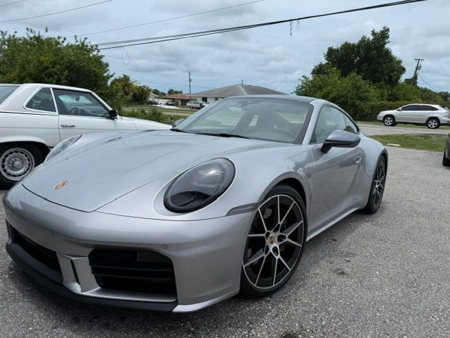 Silver Porsche 911 parked outdoors on a gravel lot under cloudy skies