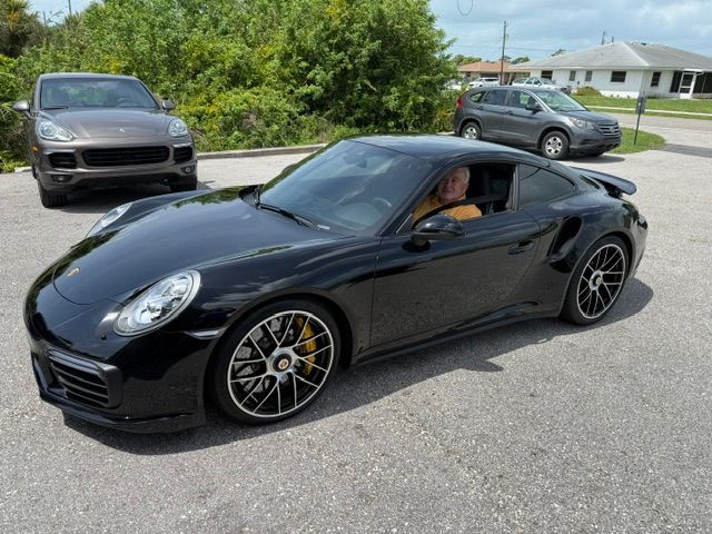 Black Porsche sports car parked on a suburban street with a driver visible in the window.