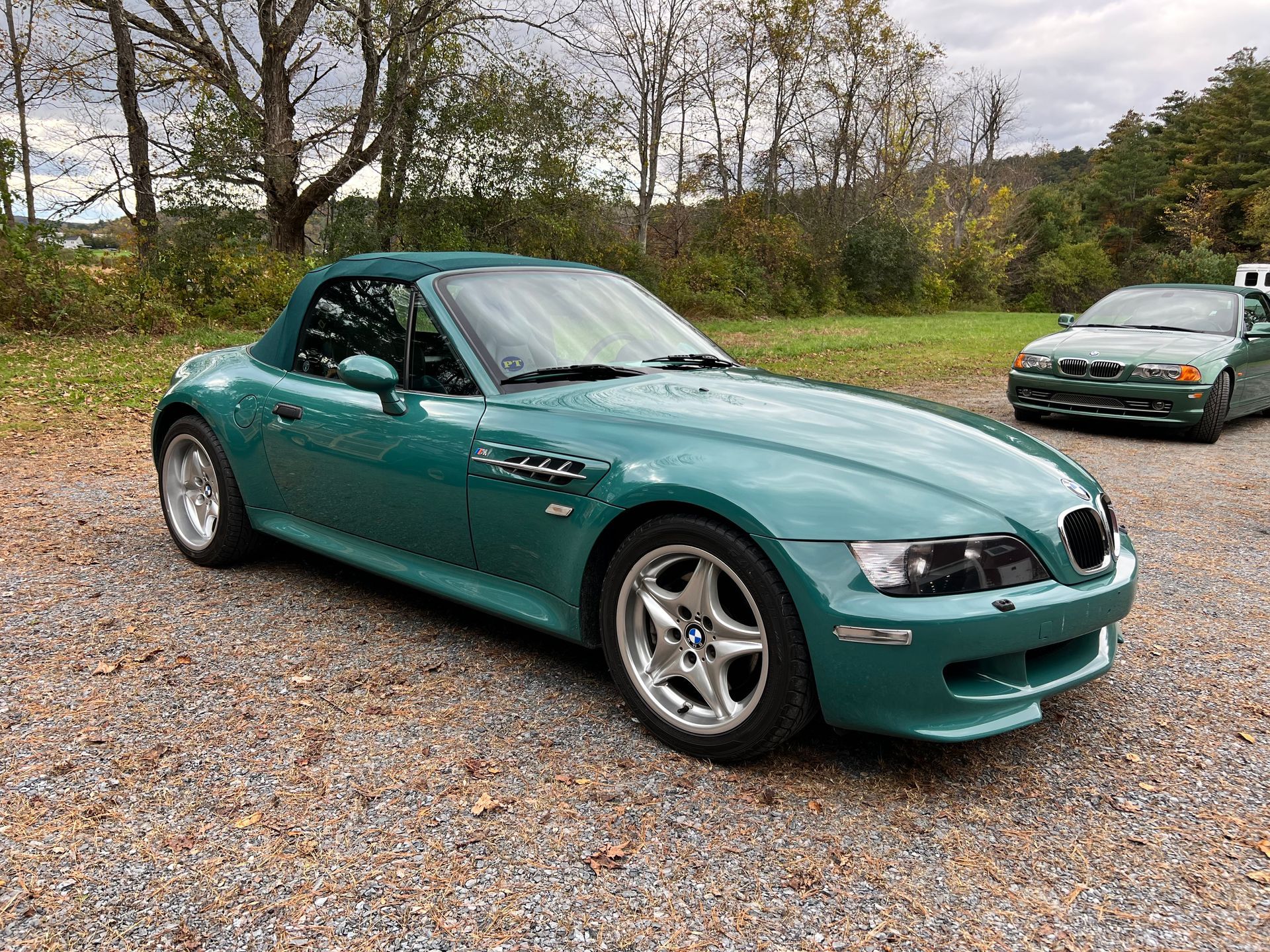 A green bmw z3 convertible is parked in a gravel lot.