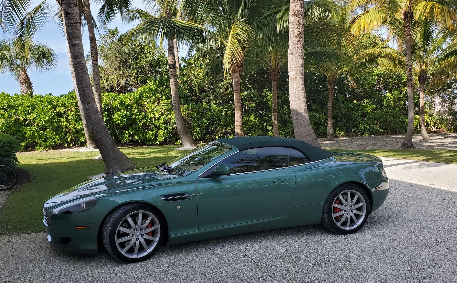 A green convertible is parked in a gravel driveway next to palm trees.