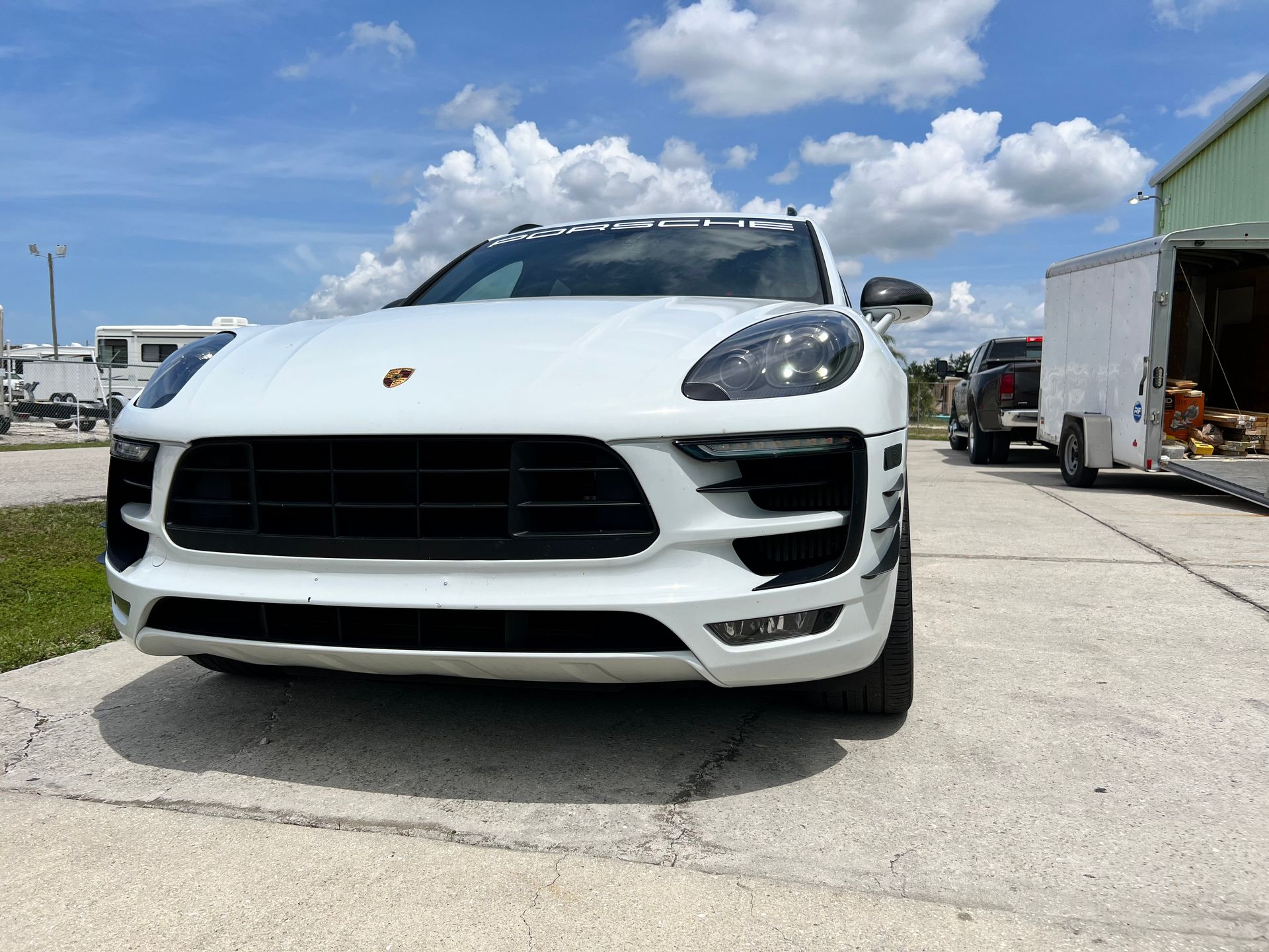 A white porsche macan is parked in a parking lot next to a trailer.