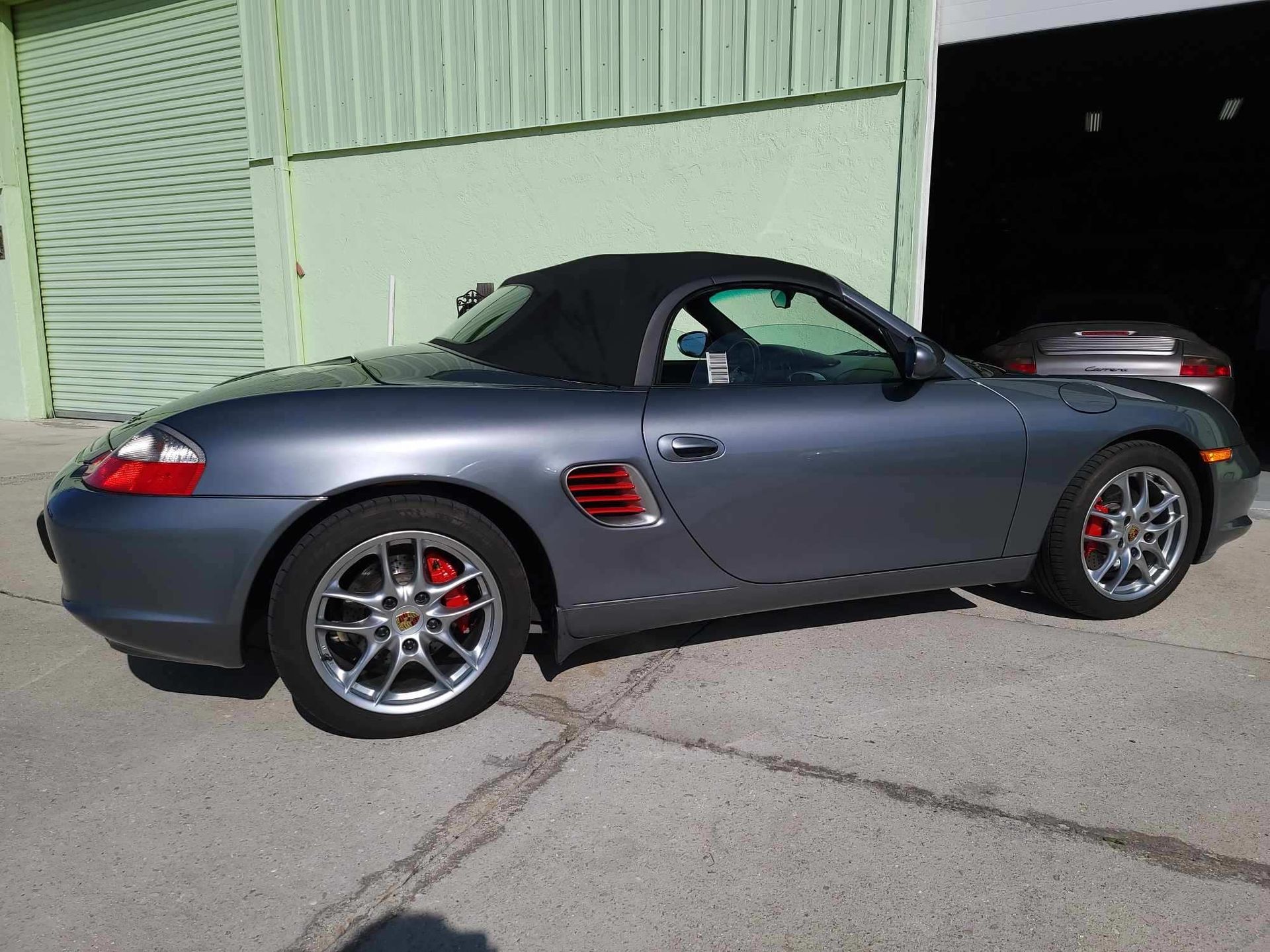 A gray porsche boxster is parked in front of a garage.