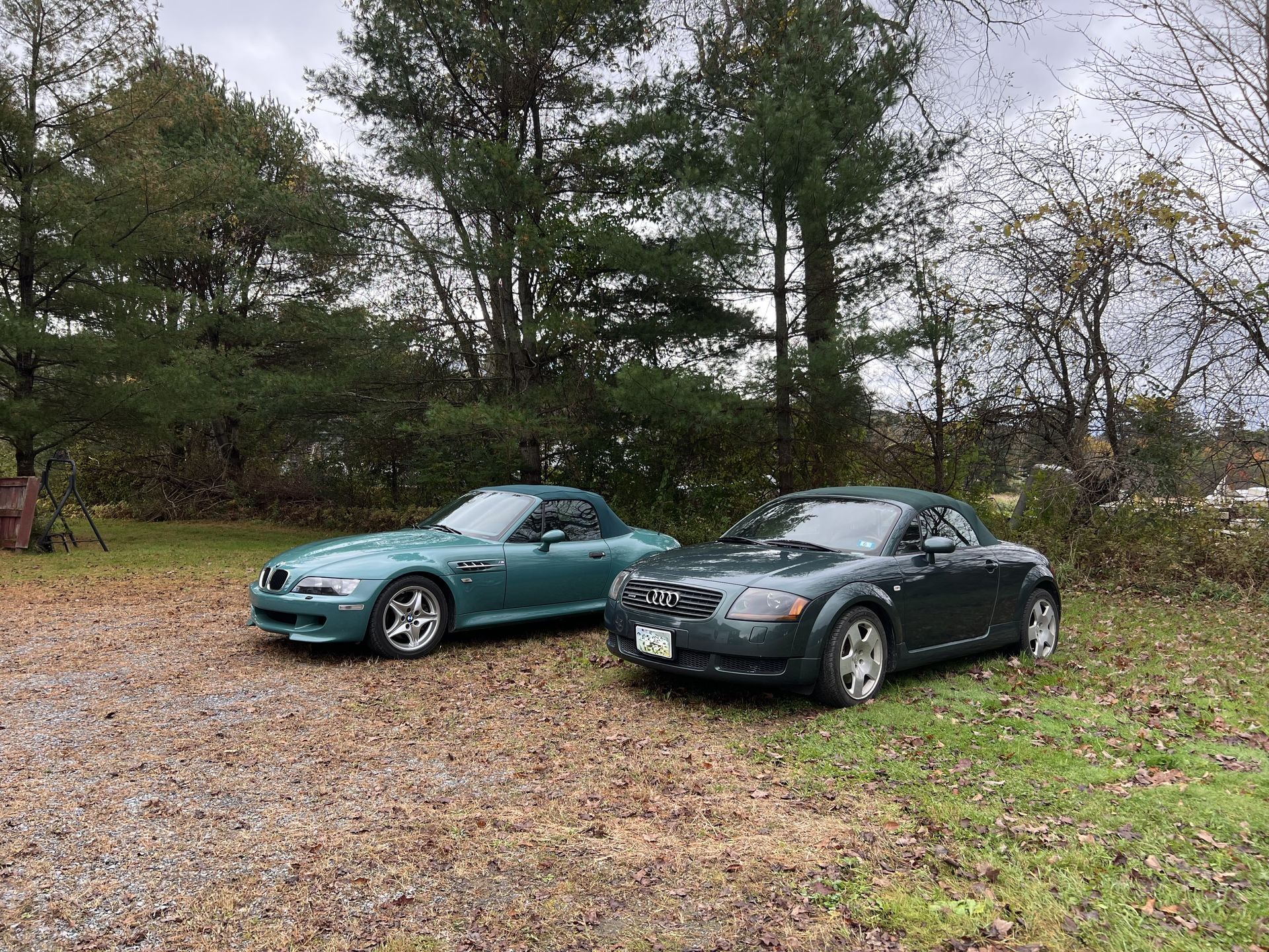 Two sports cars are parked next to each other in a gravel lot.