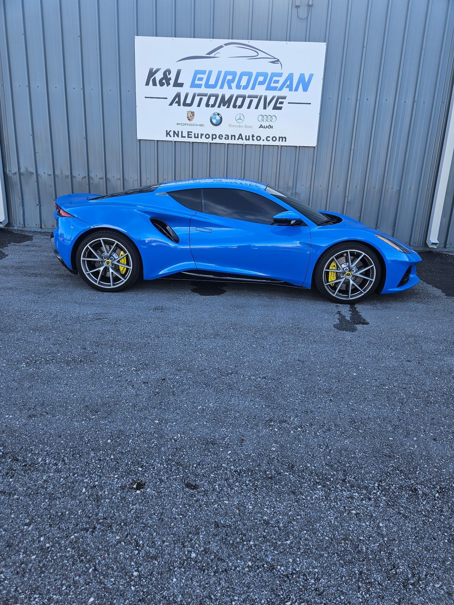 A blue sports car is parked in front of a building next to a sign.