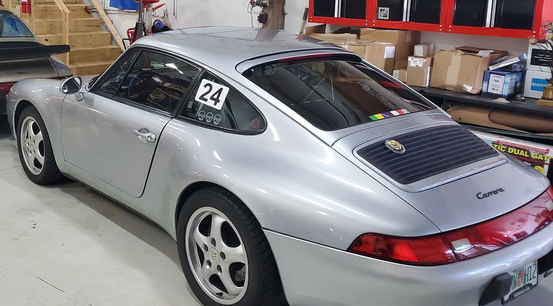 A silver porsche with the number 24 on the back is parked in a garage.