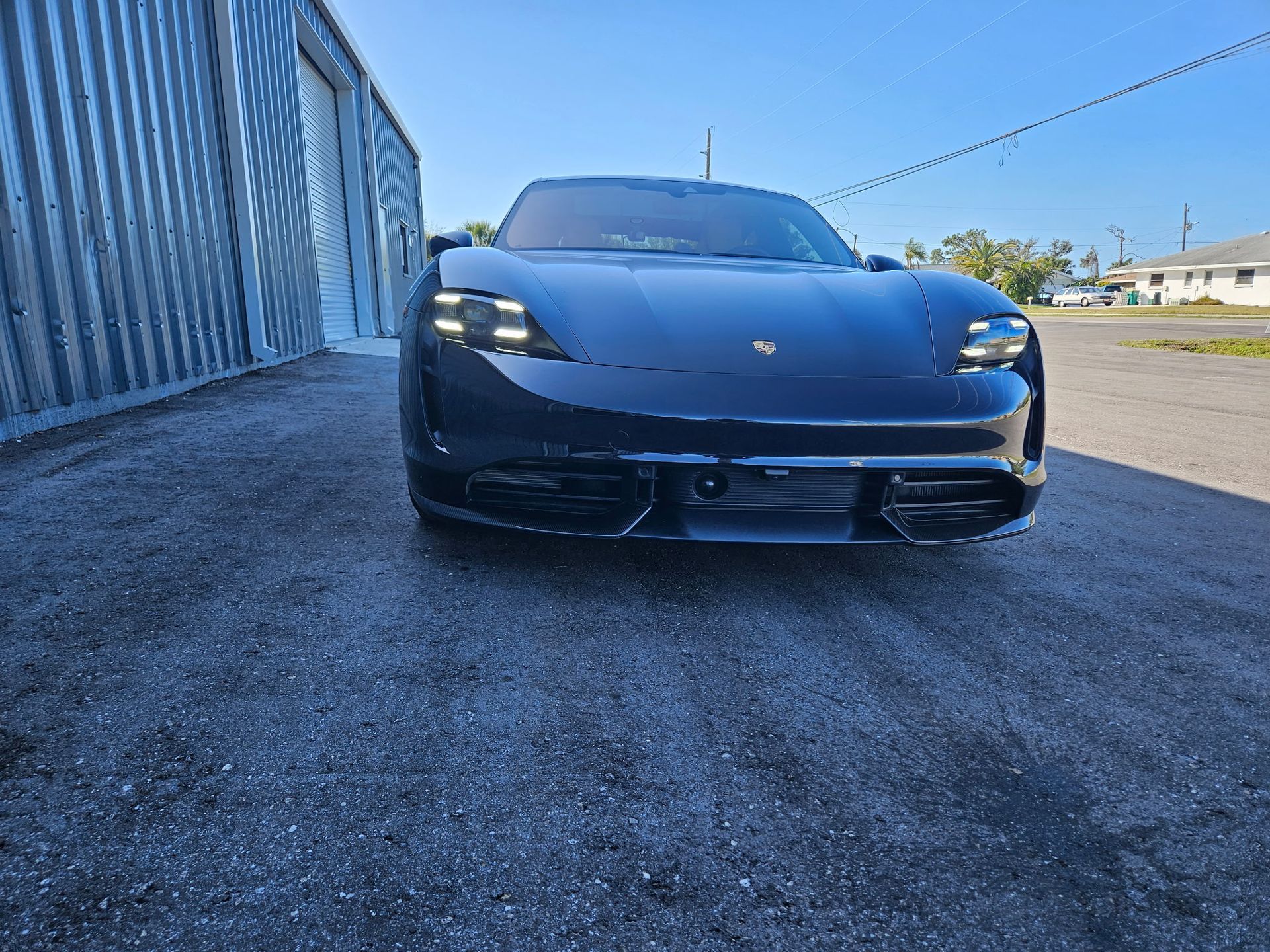 A black porsche taycan is parked in a parking lot next to a building.