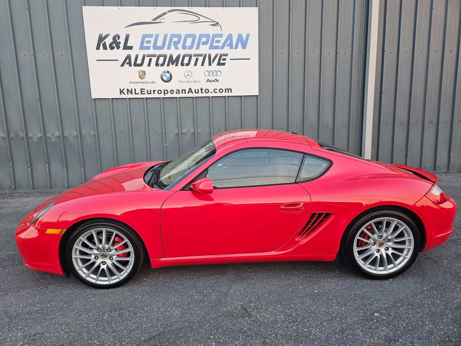 A red sports car is parked in front of a building with a sign that says k & l european automotive.