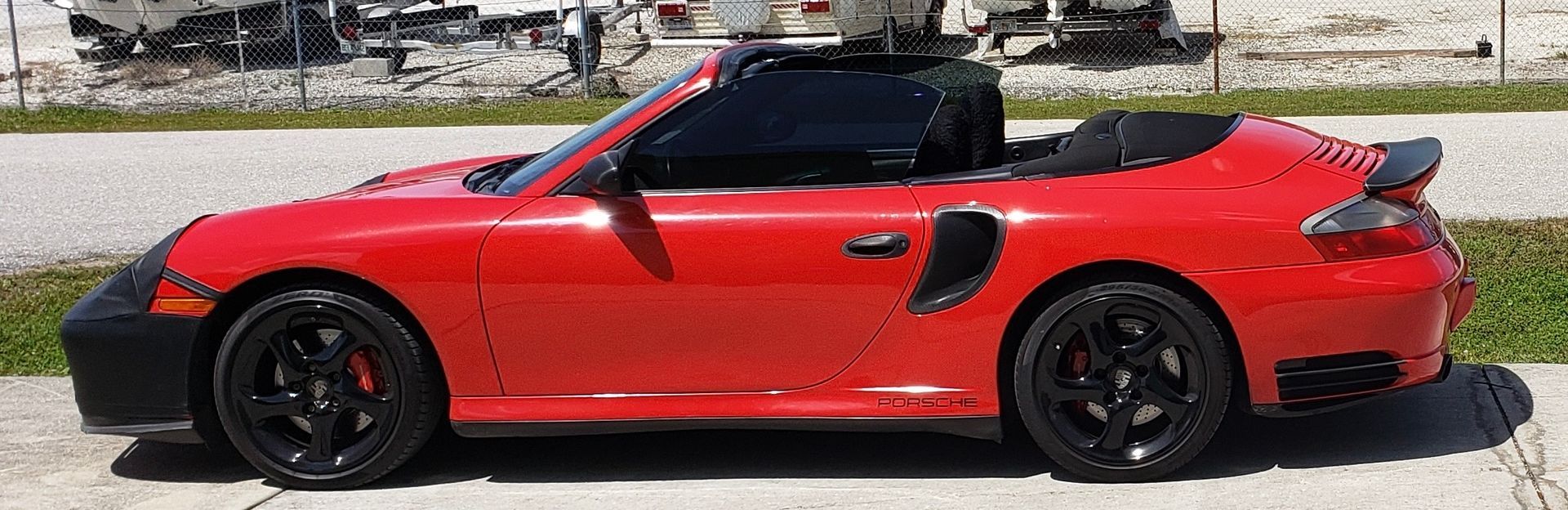 A red porsche 911 turbo convertible is parked on the side of the road.