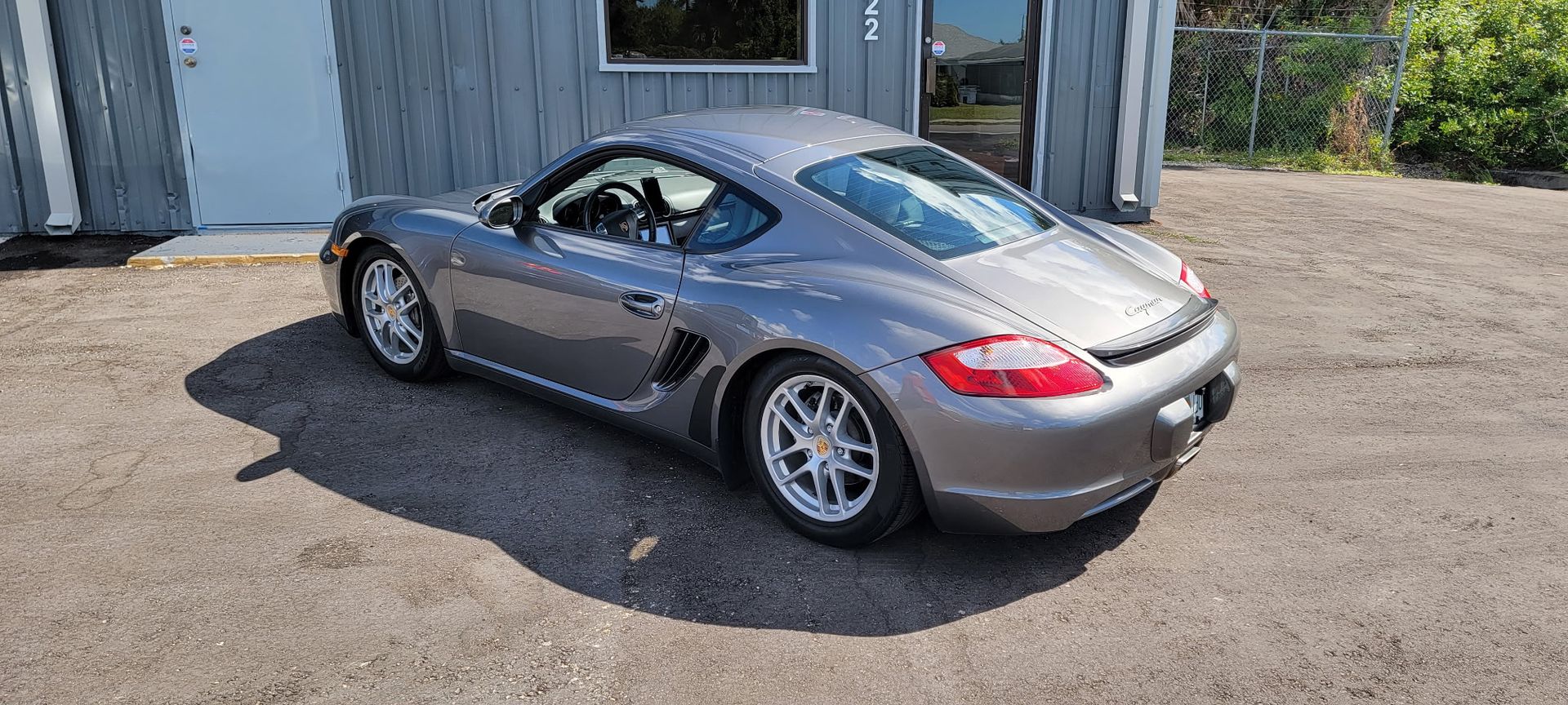 A silver porsche boxster is parked in a parking lot in front of a building.