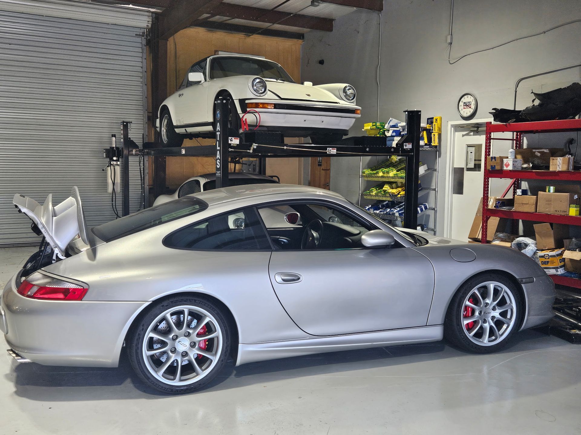 A silver car is parked in a garage next to a white car