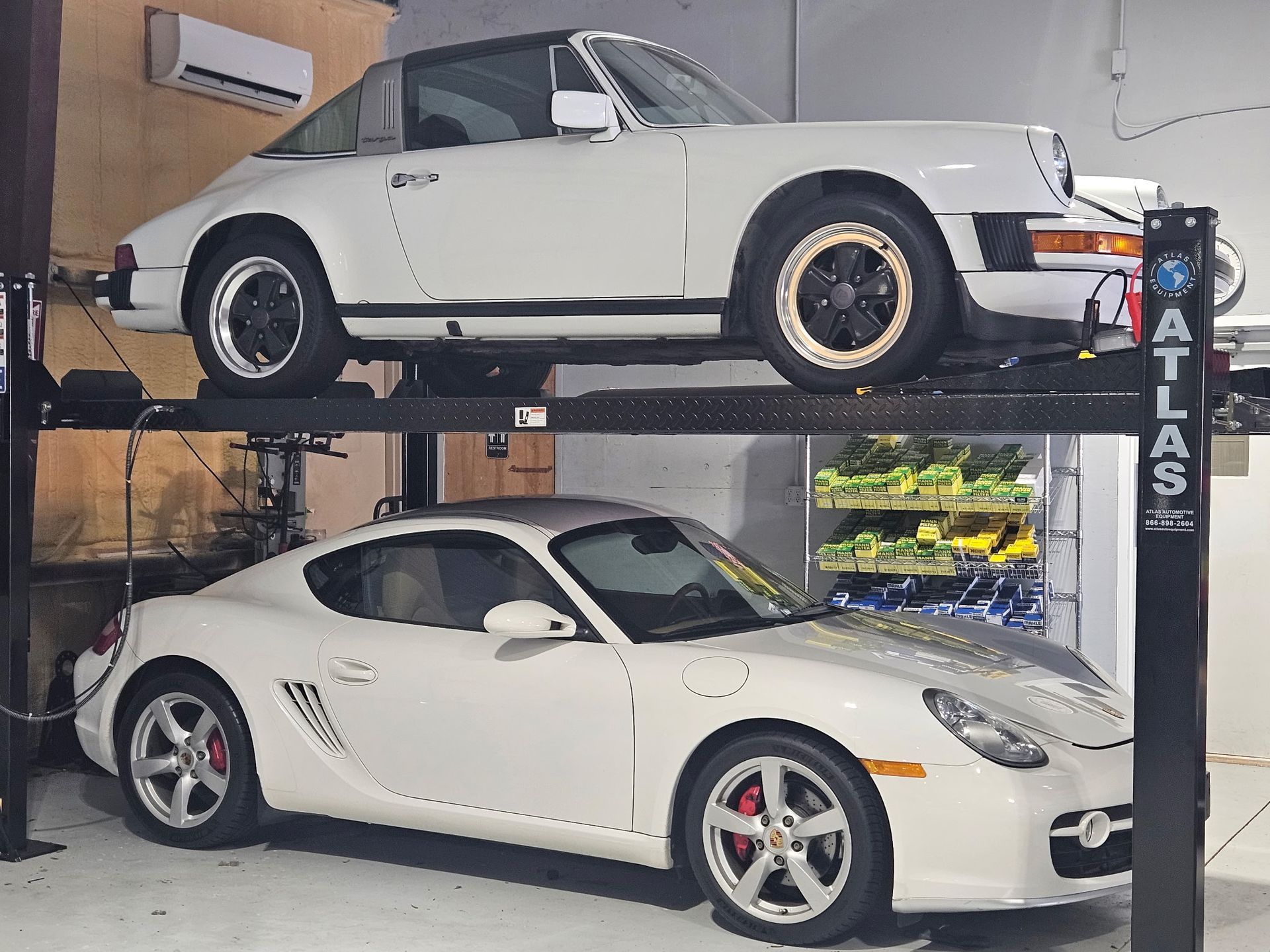 Two white cars are parked on a lift that says atlas