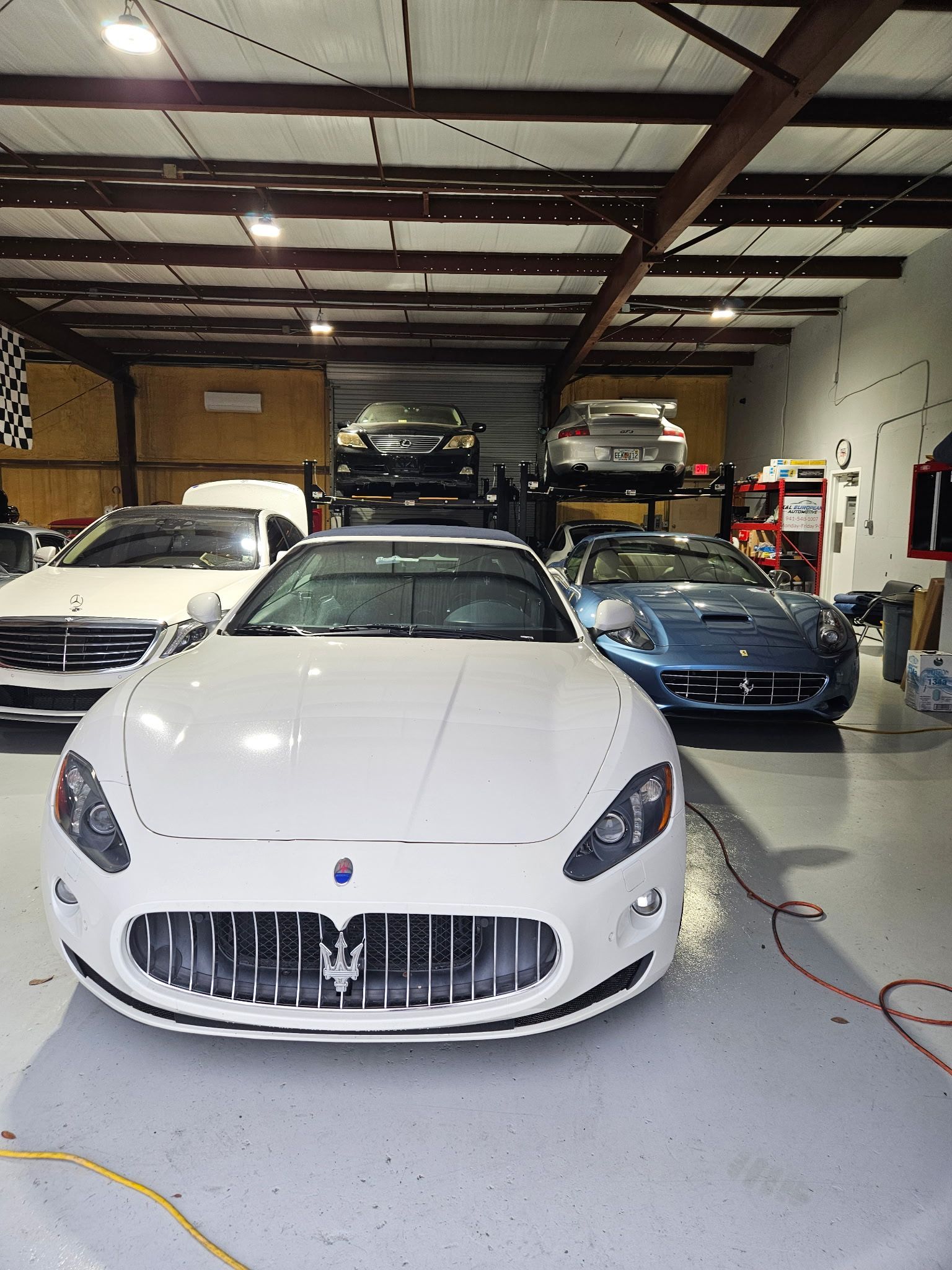 A white maserati is parked in a garage with other cars.
