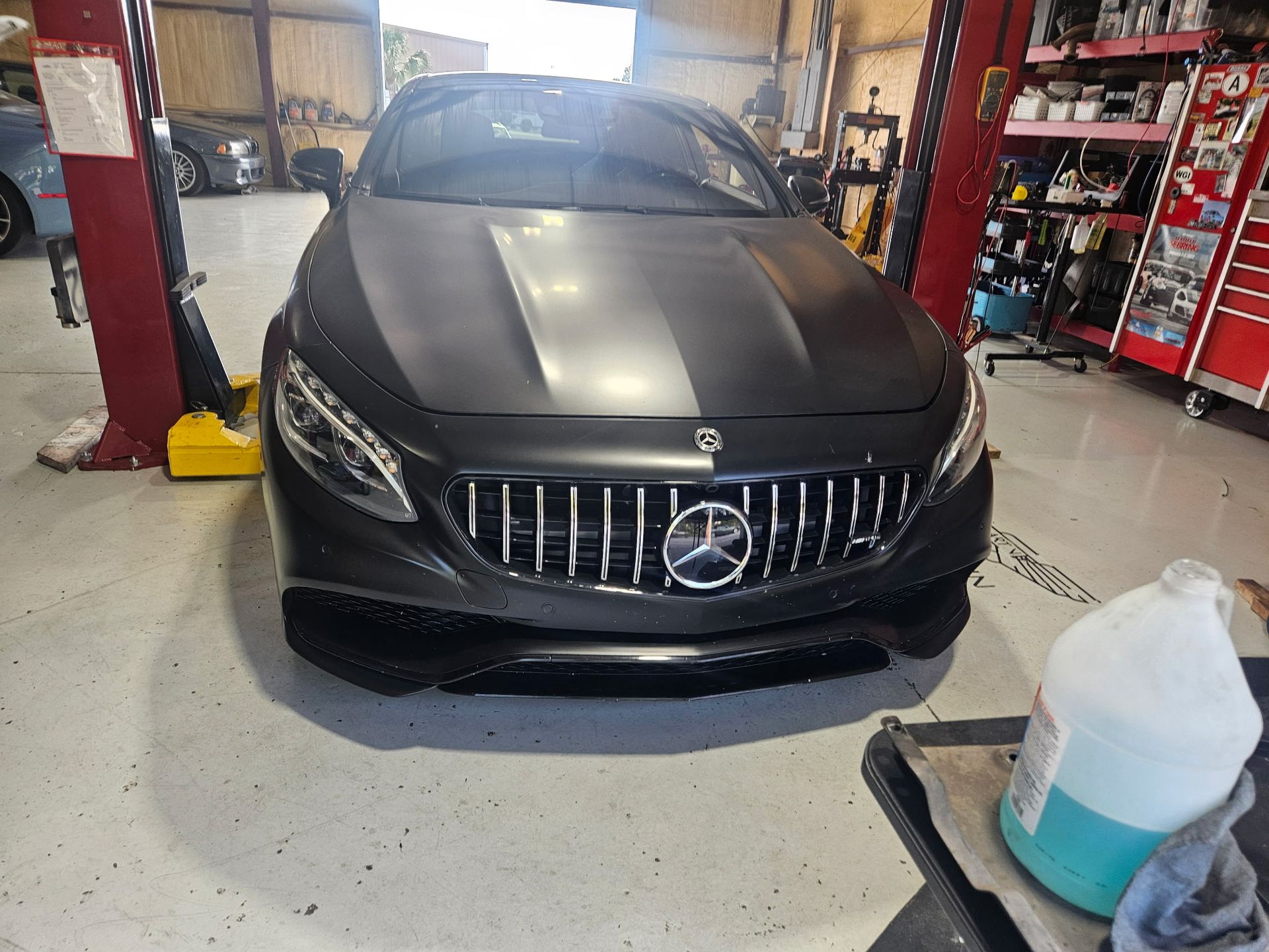 A black mercedes benz is parked in a garage next to a gallon of water.
