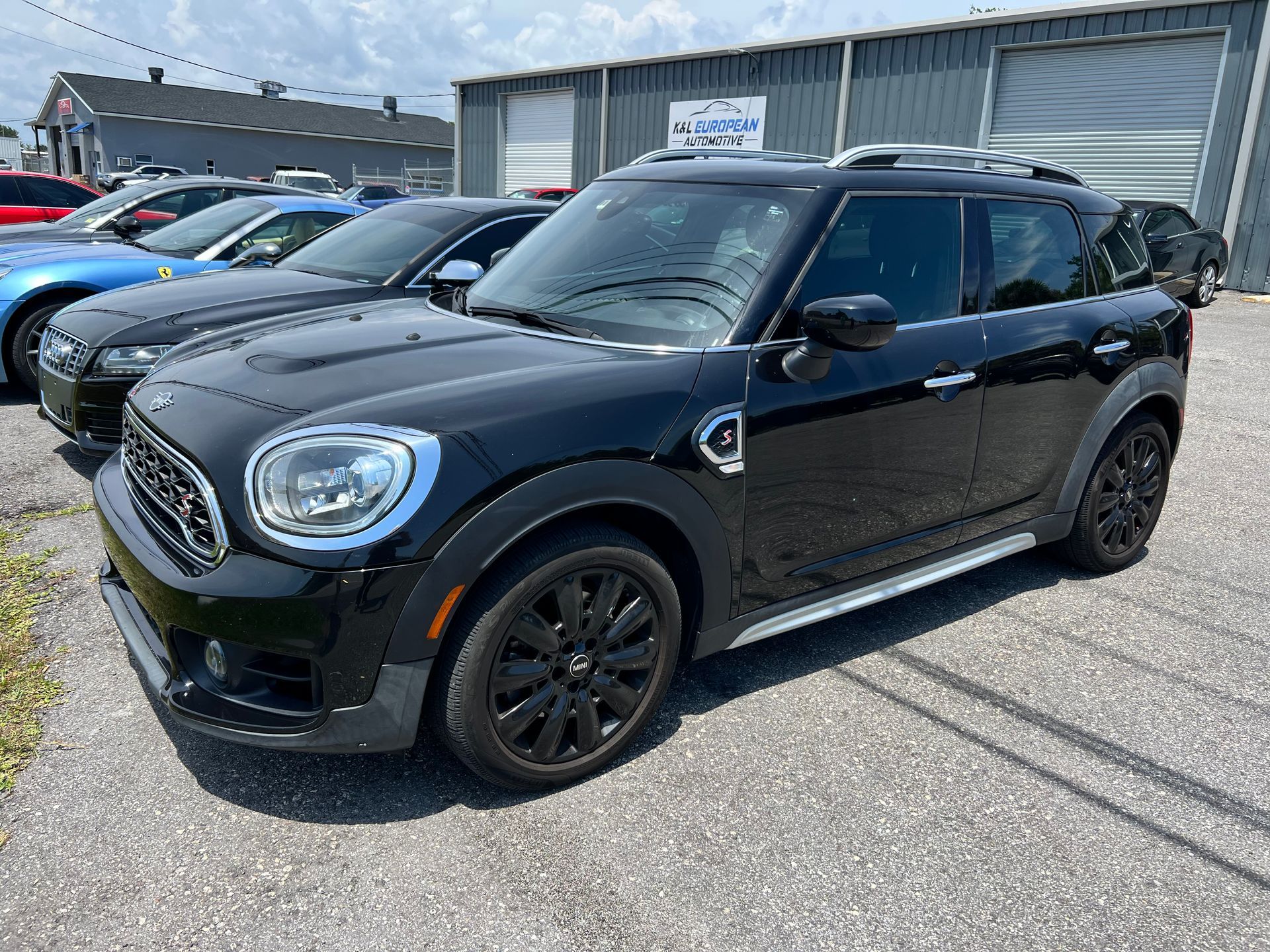 A black mini cooper countryman is parked in a lot in front of a building.