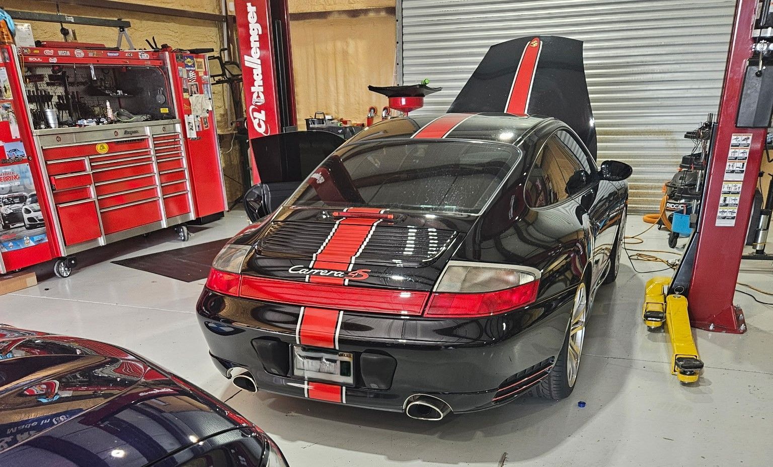 A black car with red and white stripes is parked in a garage.