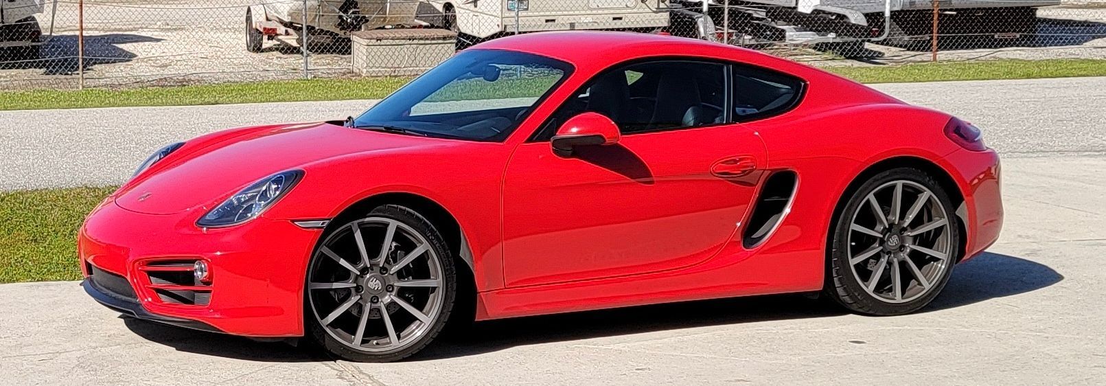 A red porsche boxster is parked on the side of the road.