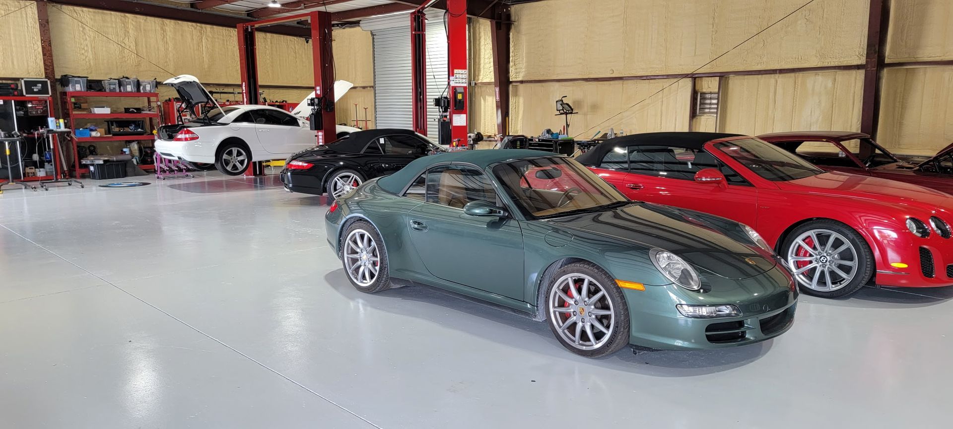 A green car is parked in a garage next to a red car.