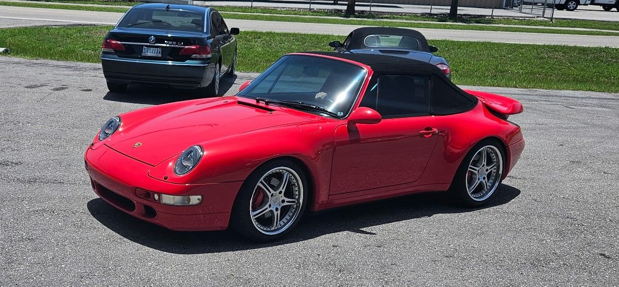 A red porsche 911 convertible is parked in a parking lot.