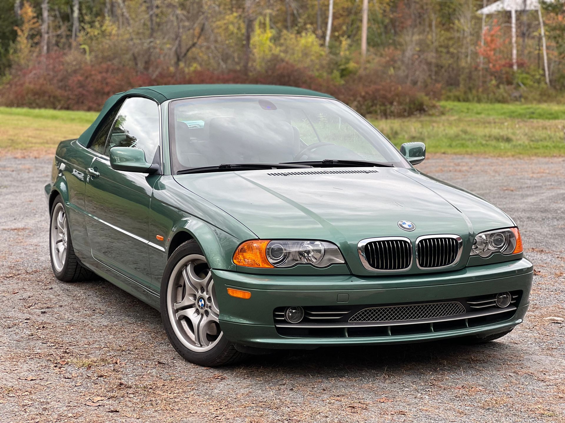 A green bmw convertible is parked in a gravel lot.