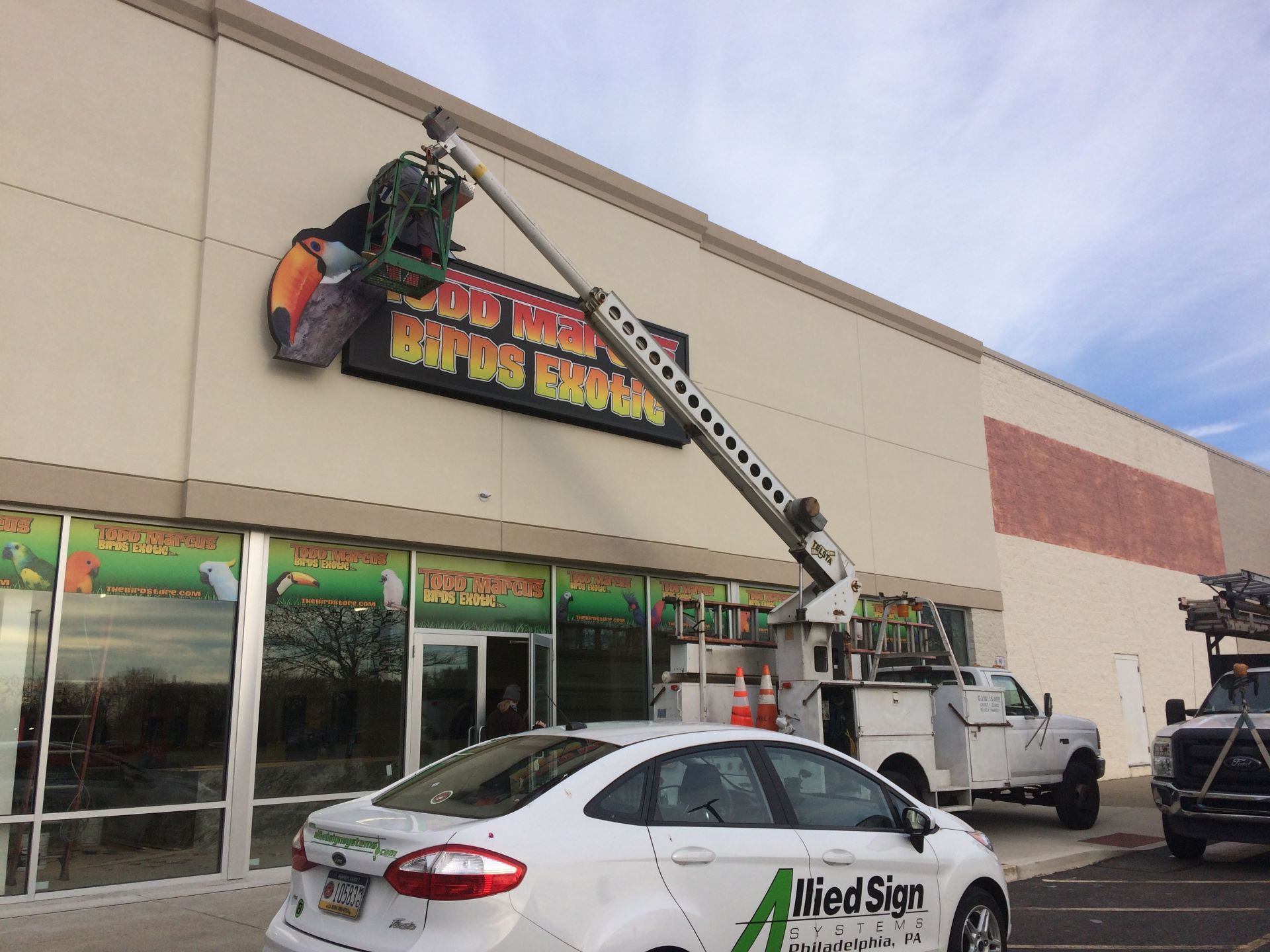A white car is parked in front of a building with a sign on it.