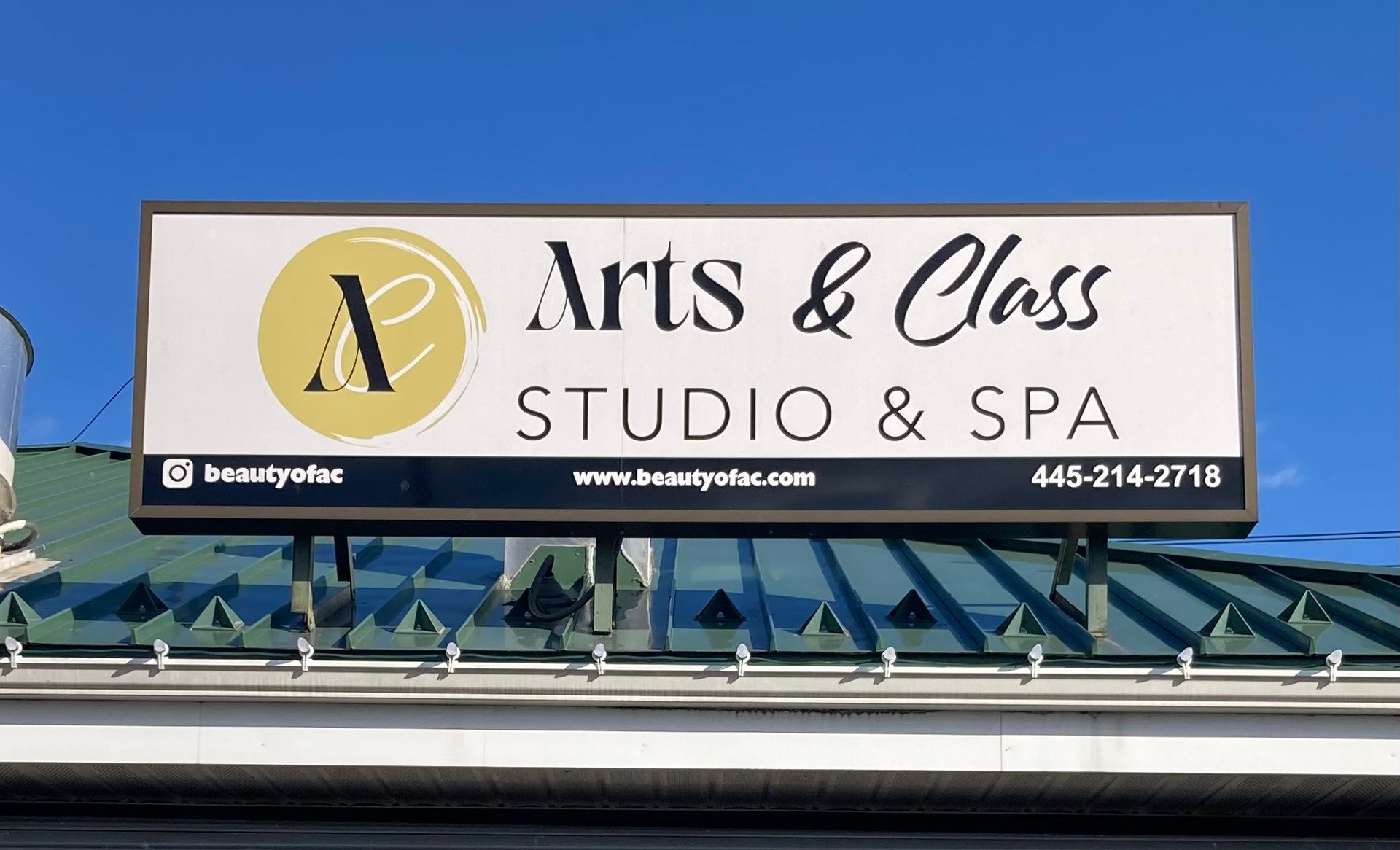 A billboard for arts & class studio & spa is hanging from the roof of a building.