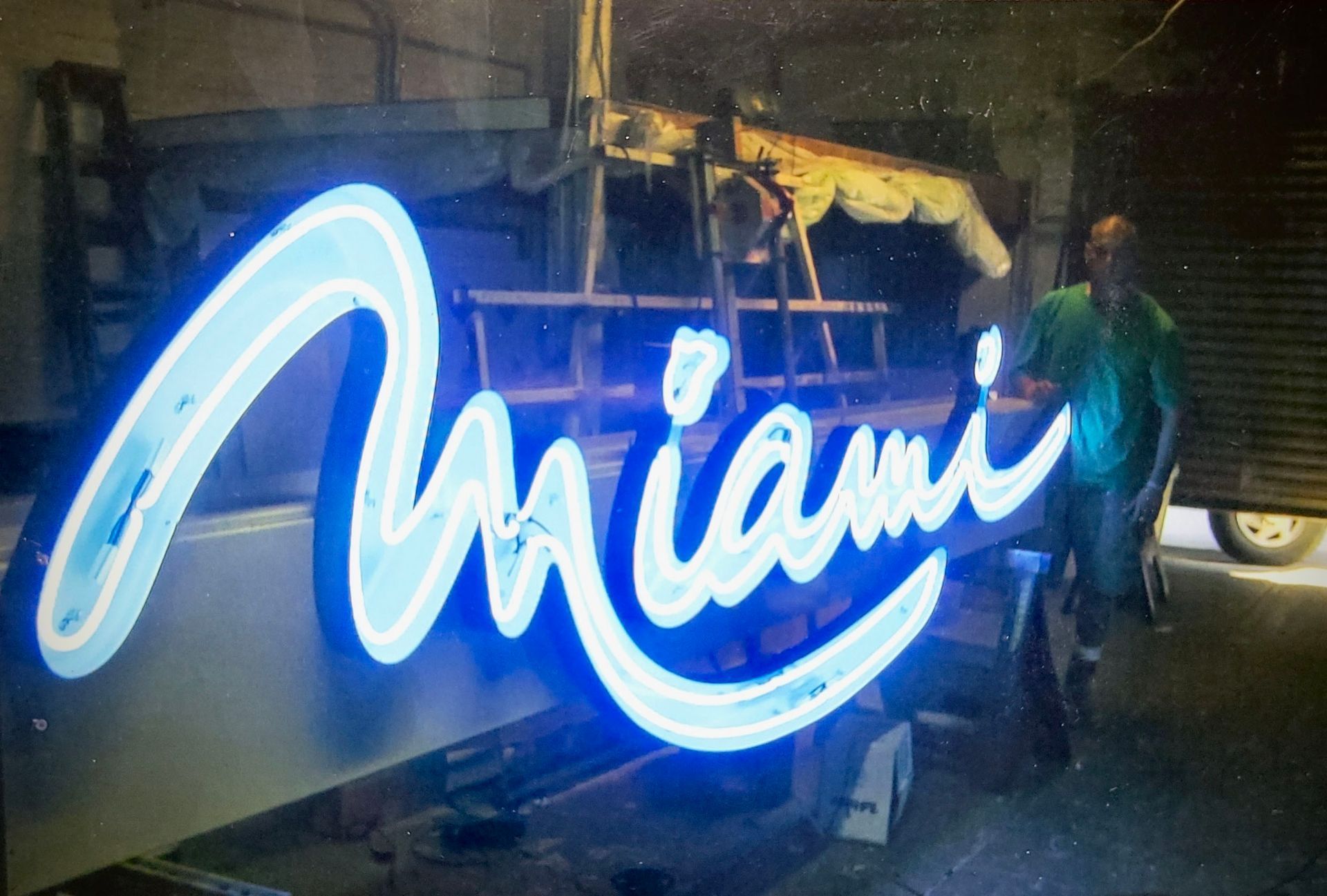 A man is standing next to a neon sign that says miami