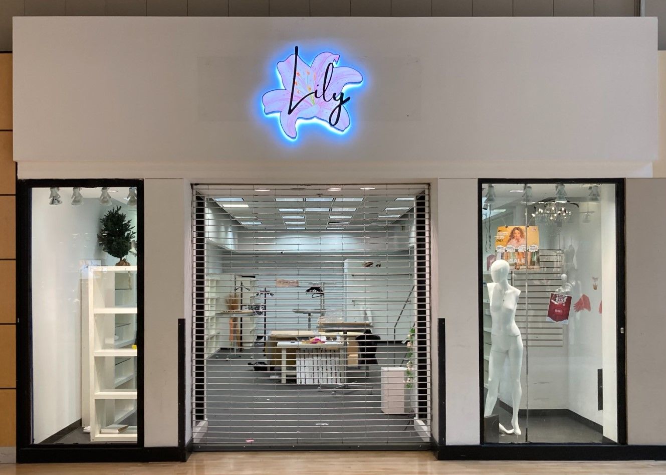 A store front with a rolling shutter and a neon sign.