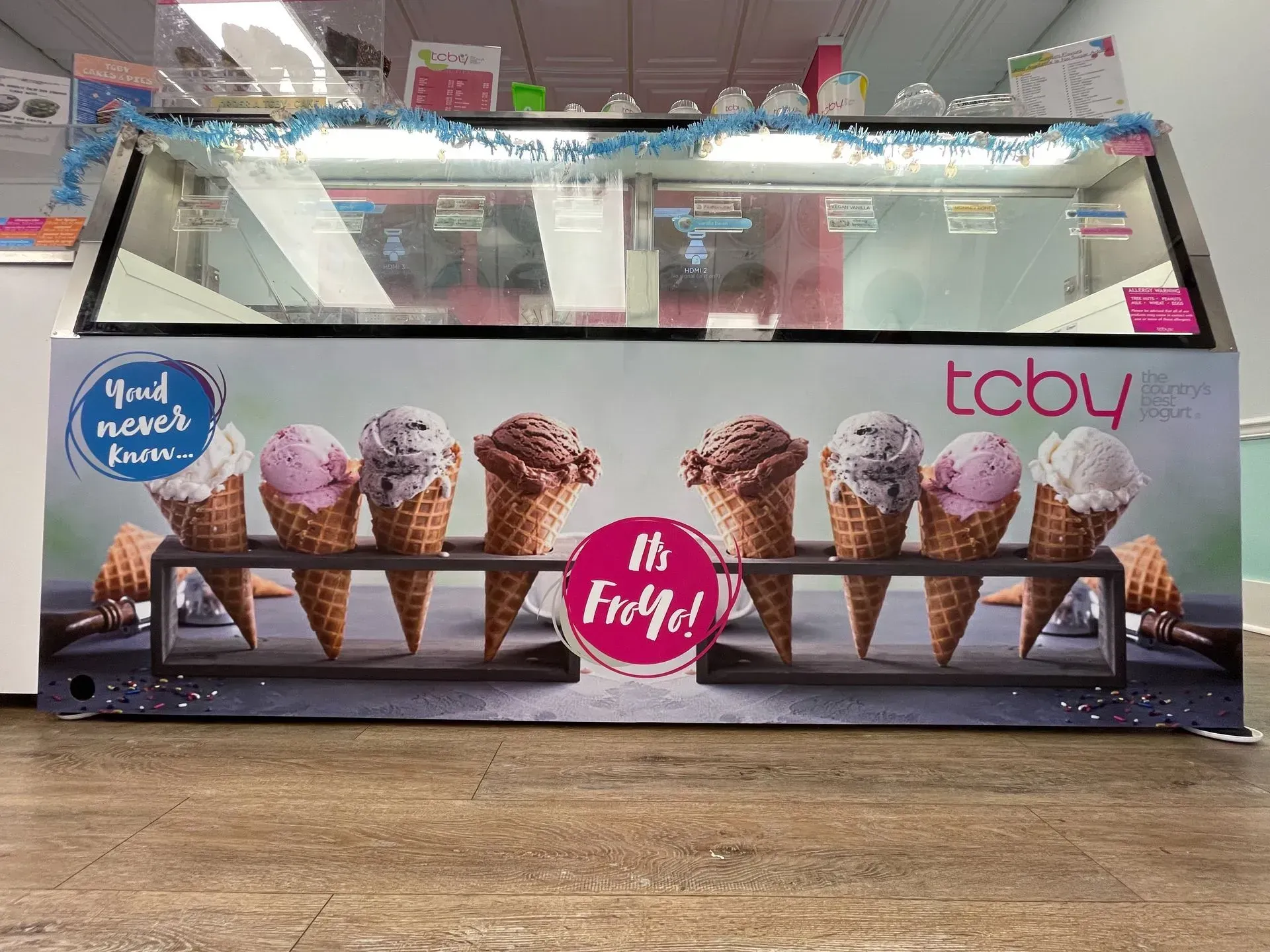 A display case filled with ice cream cones is sitting on a wooden floor.
