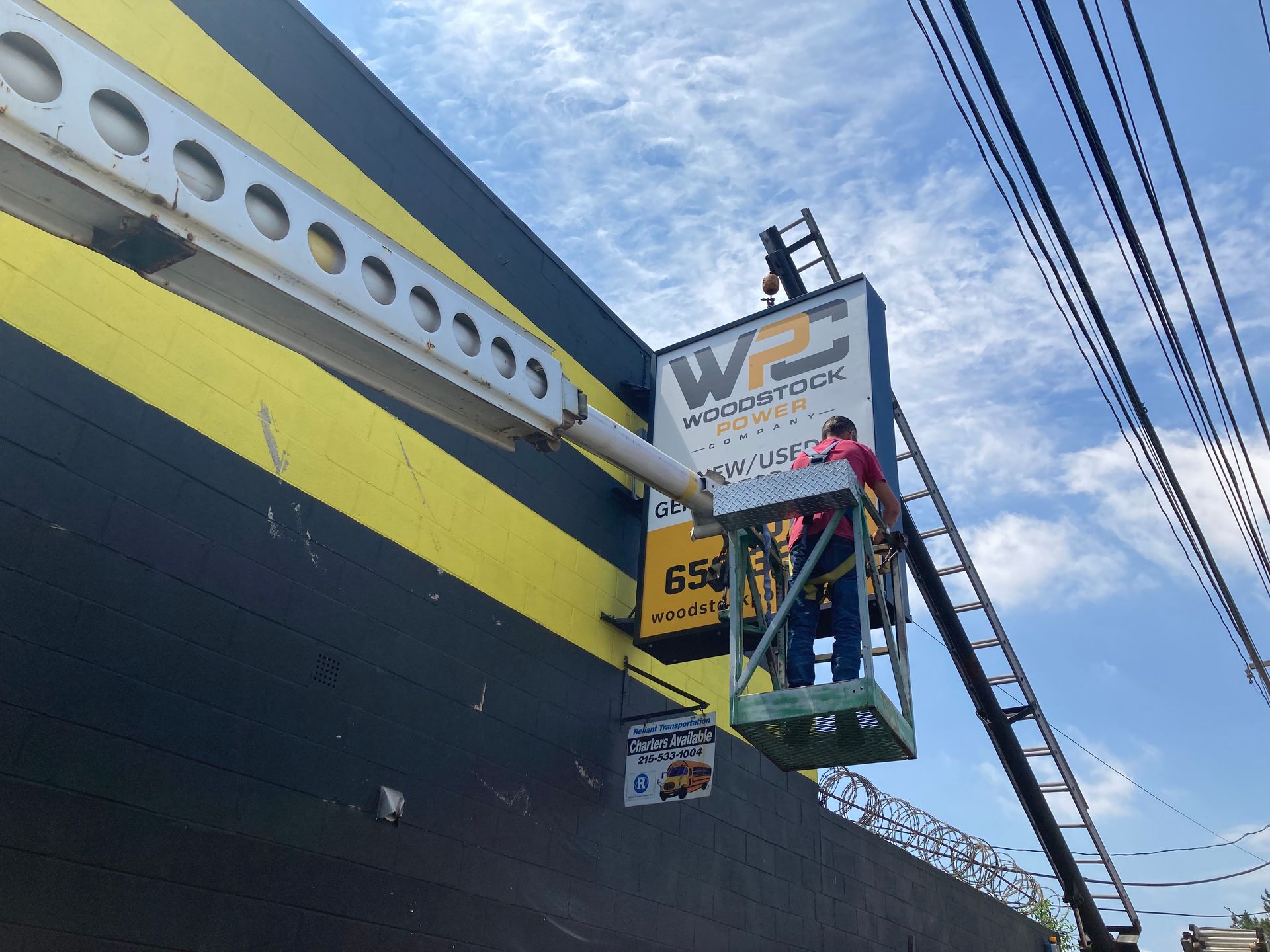 A man on a ladder is hanging a sign on the side of a building.