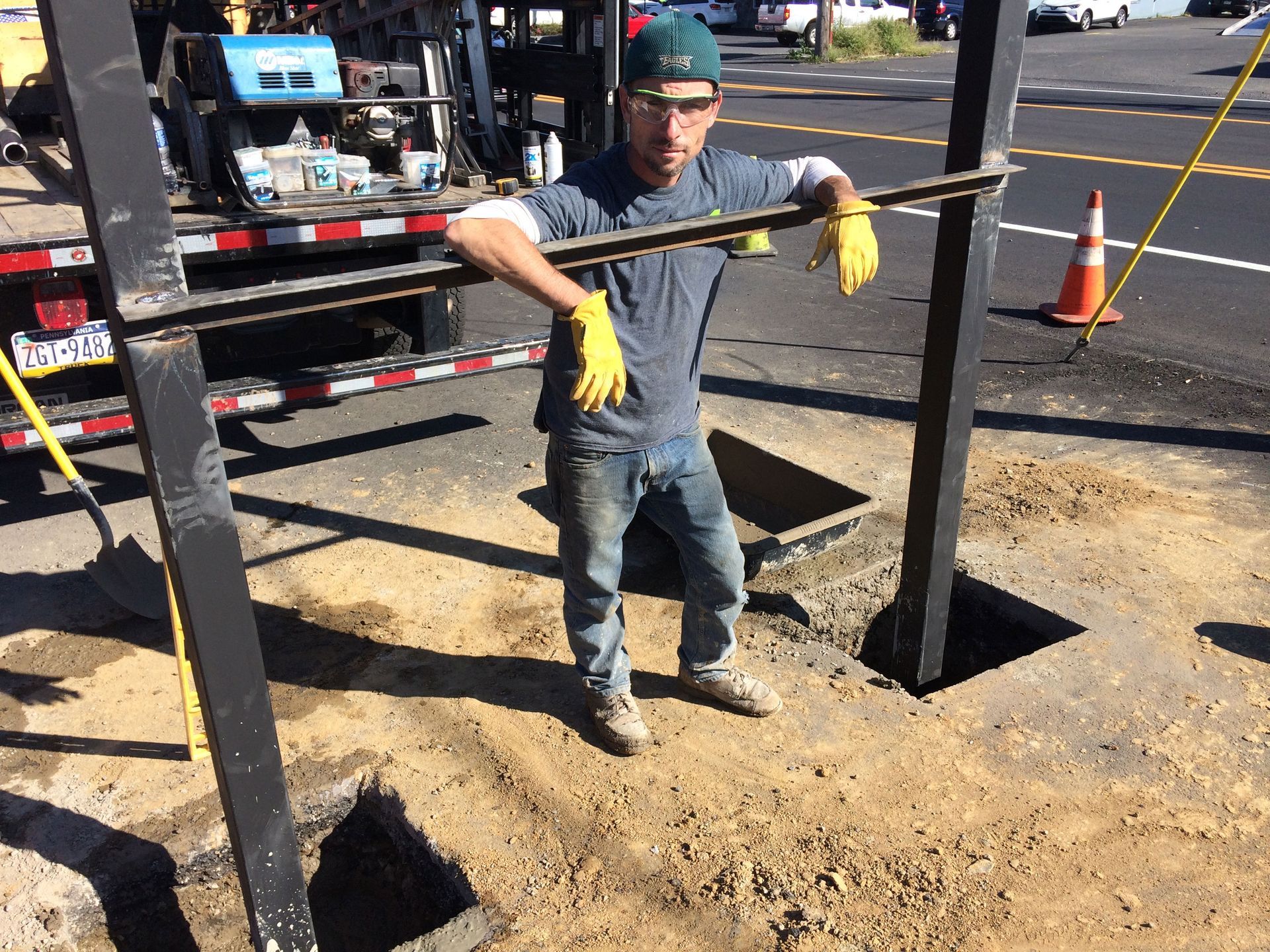 A man is kneeling down on the ground working on a pole.