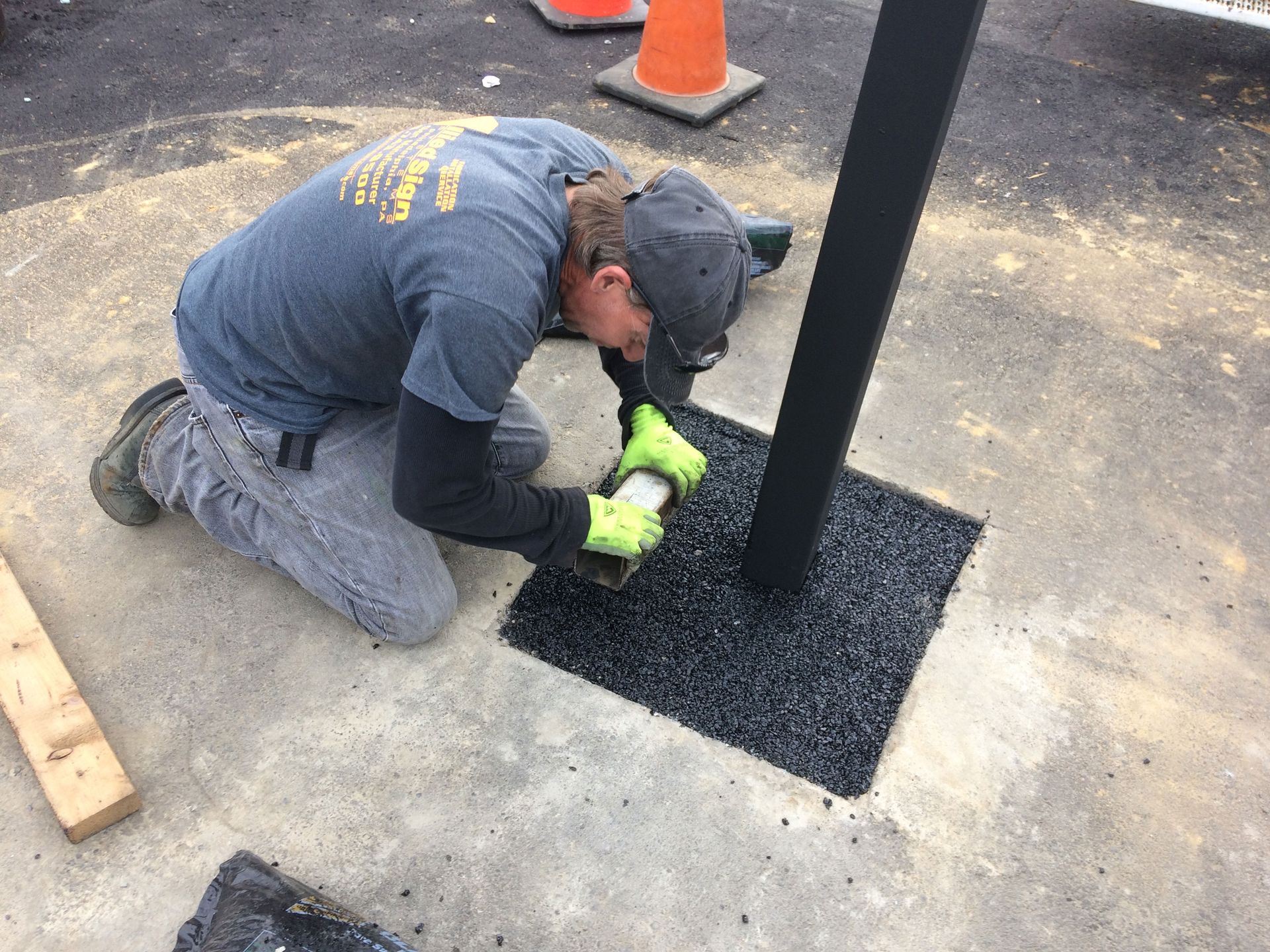 A man is kneeling down on the ground working on a pole.