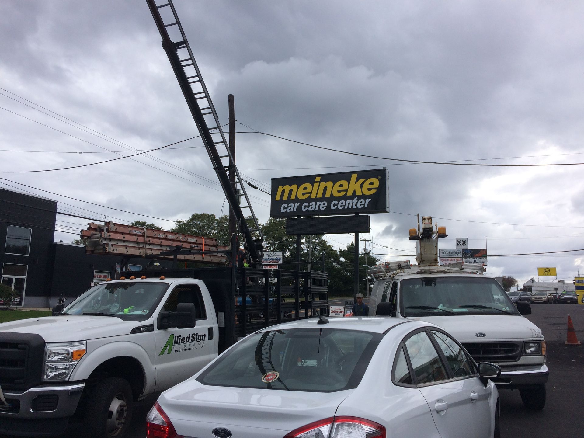A white car is parked in front of a meineke car care center sign.