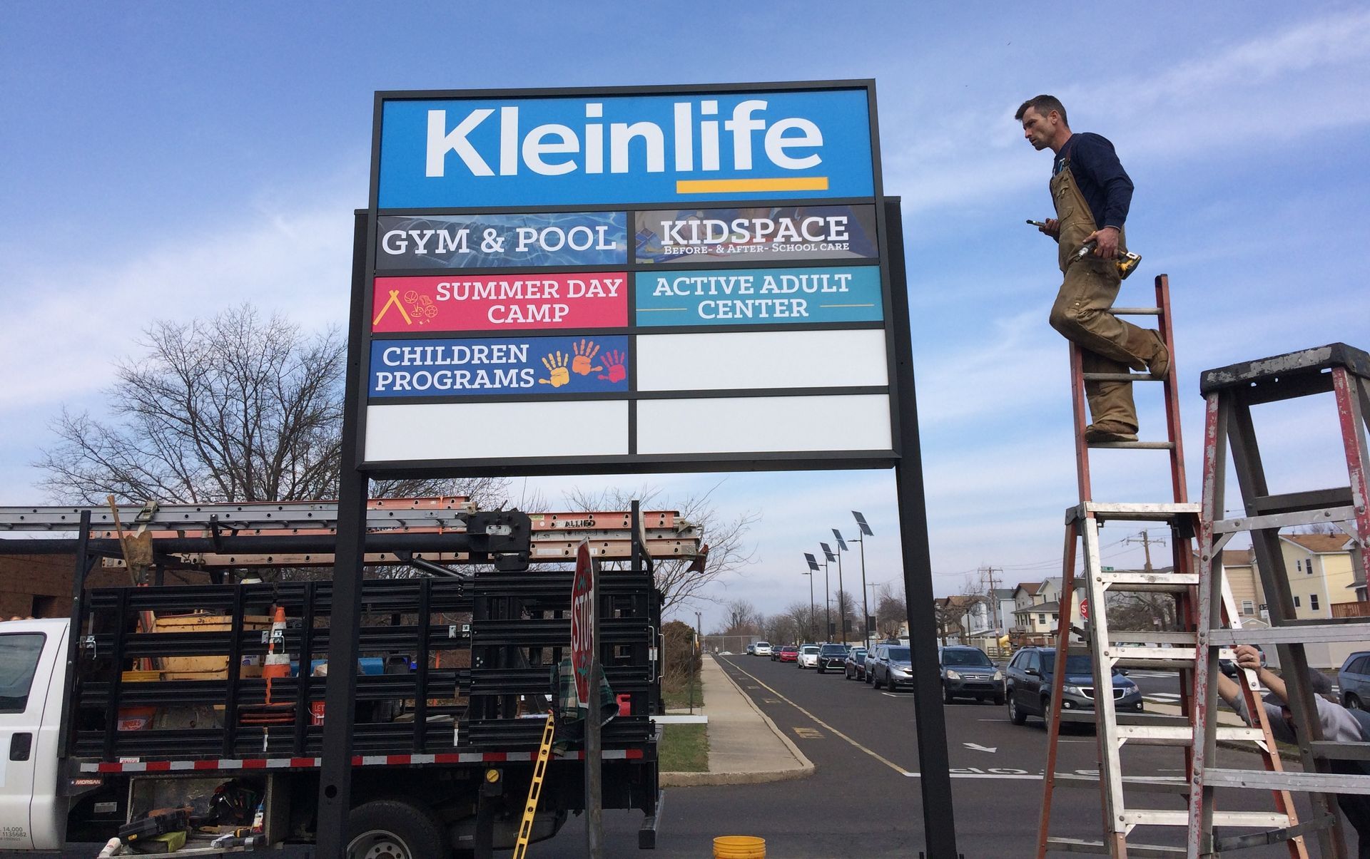 A man is standing on a ladder next to a sign that says kleinlife