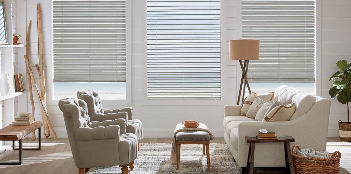 Bright living room with cream sofa and armchairs, wooden coffee table, woven rug, and large windows with blinds