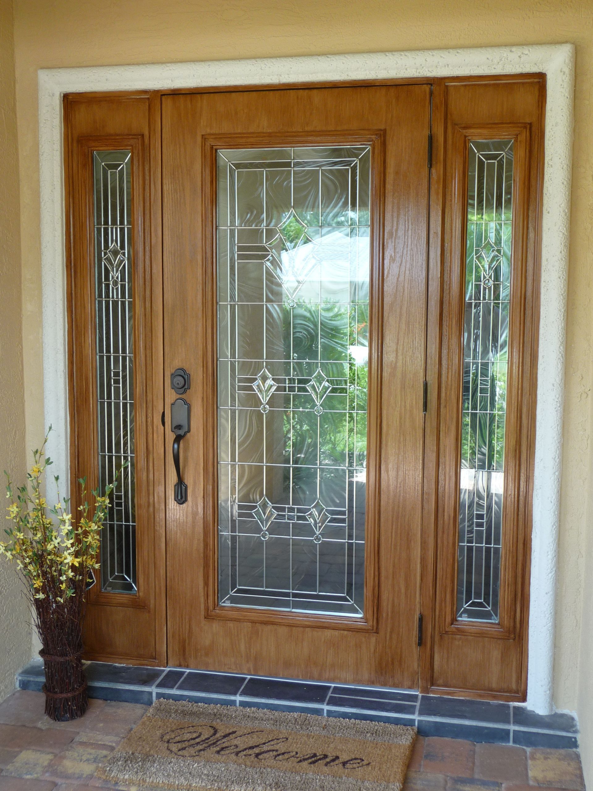 A wood-toned front door with glass panels on the sides, featuring decorative glass inserts and a black handle.