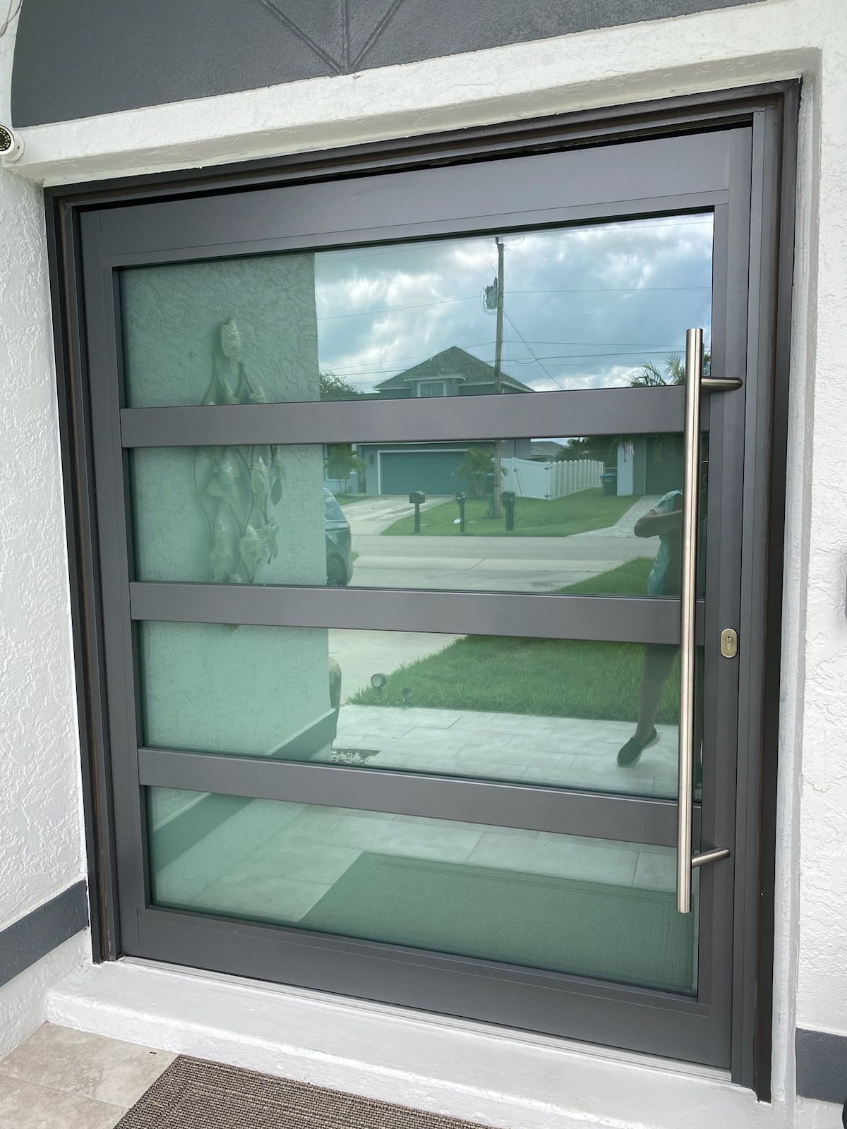 Modern gray sliding glass door with horizontal bars and a vertical handle, reflecting a suburban street.