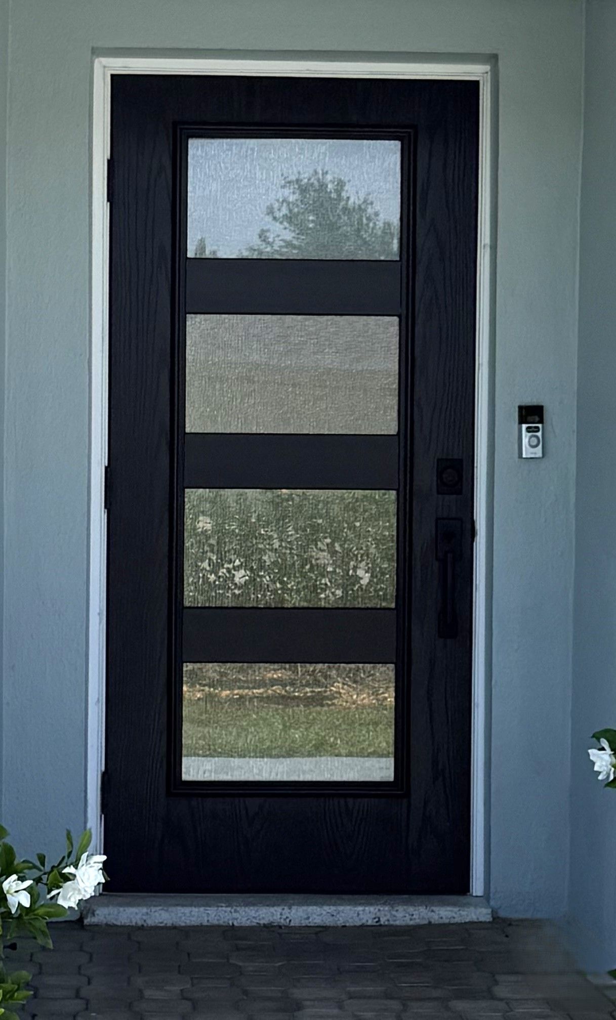 Modern black front door with three frosted glass panels in a gray exterior wall.