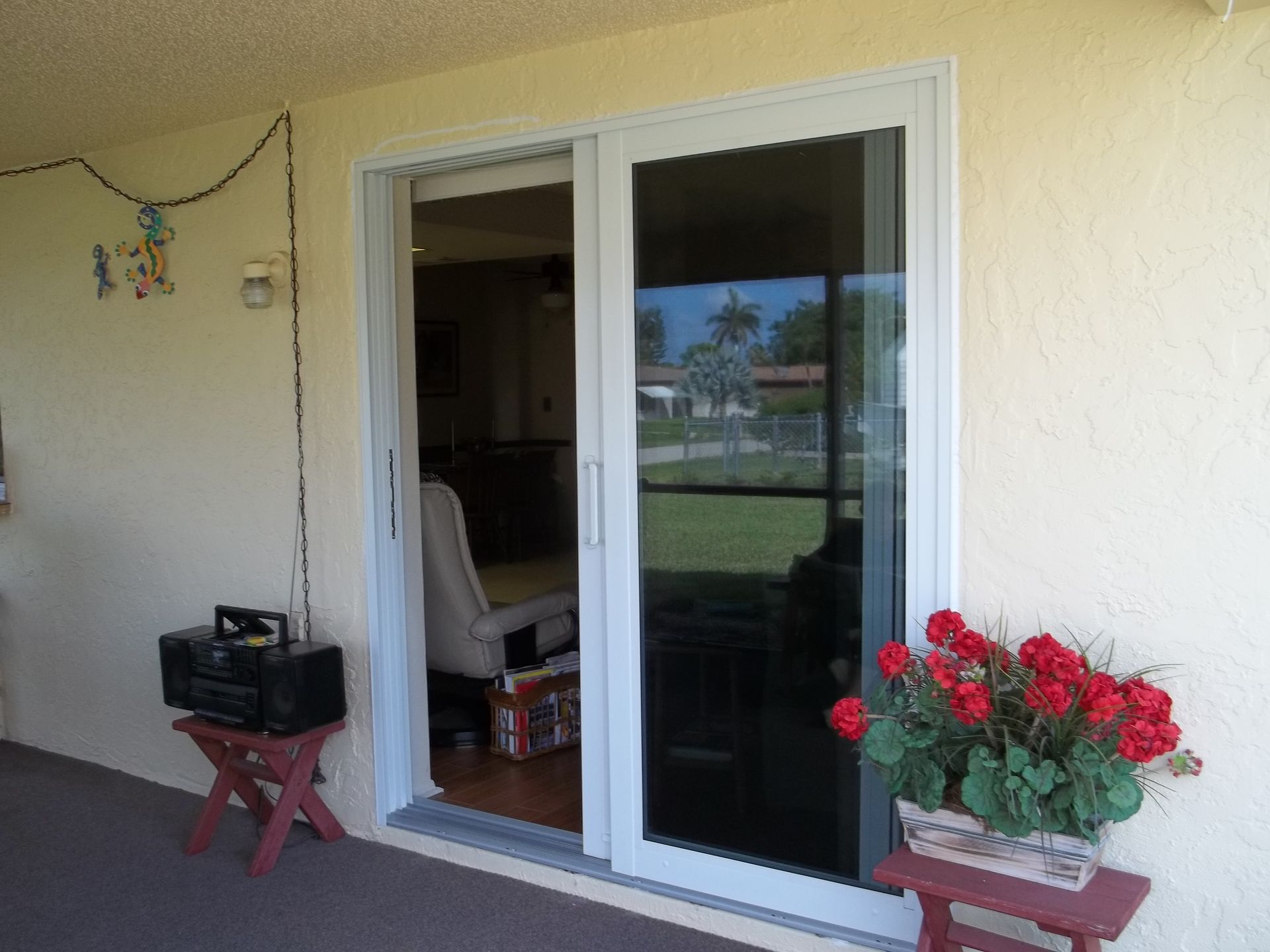 A sliding glass door on a beige wall, flanked by small stands holding a boombox on the left and red flowers on the right.