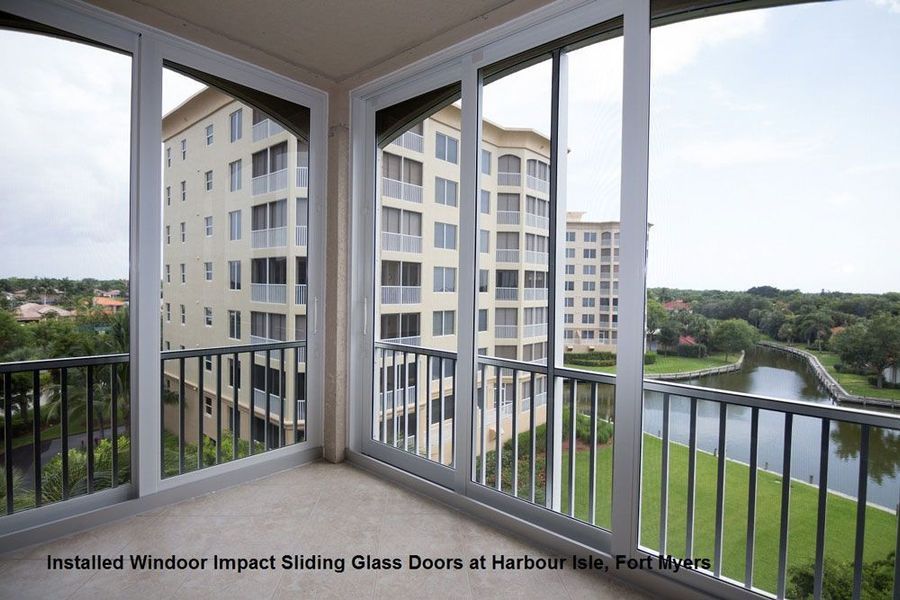White impact sliding glass doors installed on a balcony overlooking a lake and apartment buildings in Fort Myers.