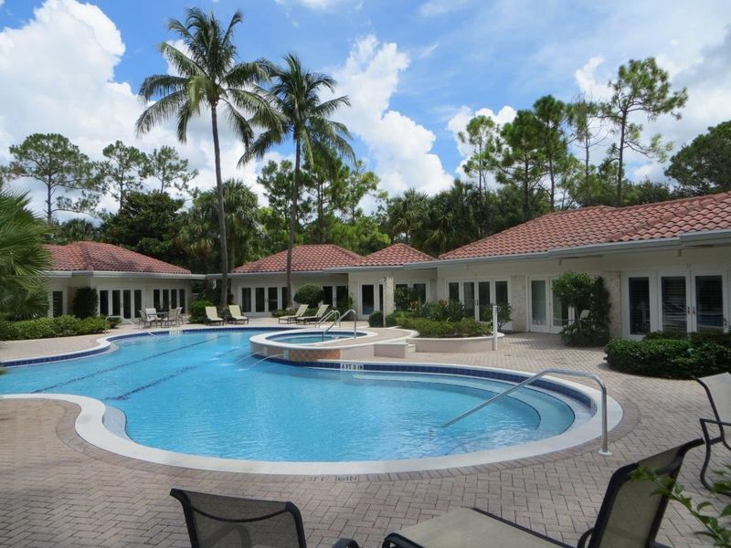 A resort-style swimming pool with a spa in a courtyard surrounded by palm trees and single-story buildings.