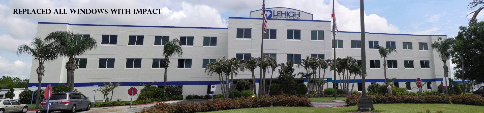 A white, multi-story commercial building with blue trim and new windows, situated behind a green lawn and palm trees.