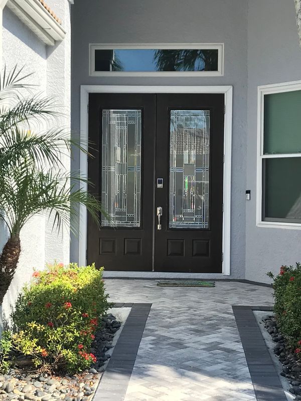 Dark double front doors with decorative glass panels and a transom window, set in a light grey home entry with a walkway.