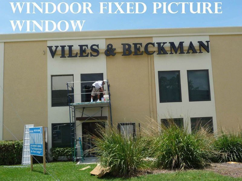 A worker on scaffolding installs or maintains a window on the exterior of the beige Viles & Beckman building.