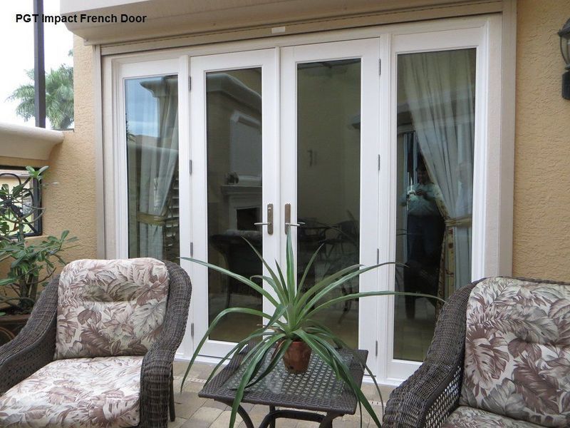 A white four-panel French door set with sidelights, located on a patio with two wicker chairs and a center table.