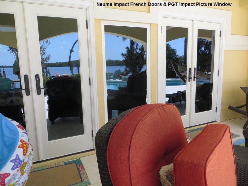 Neuma impact French doors and a PGT impact picture window overlooking a pool and waterfront at twilight.