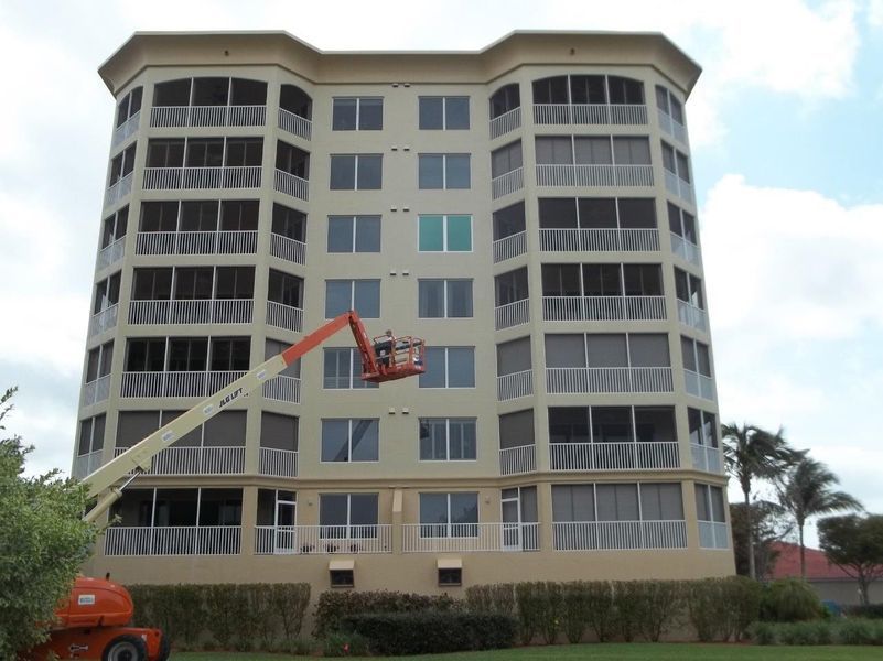 A tall beige apartment building with a construction lift parked in front, reaching toward the center stories.
